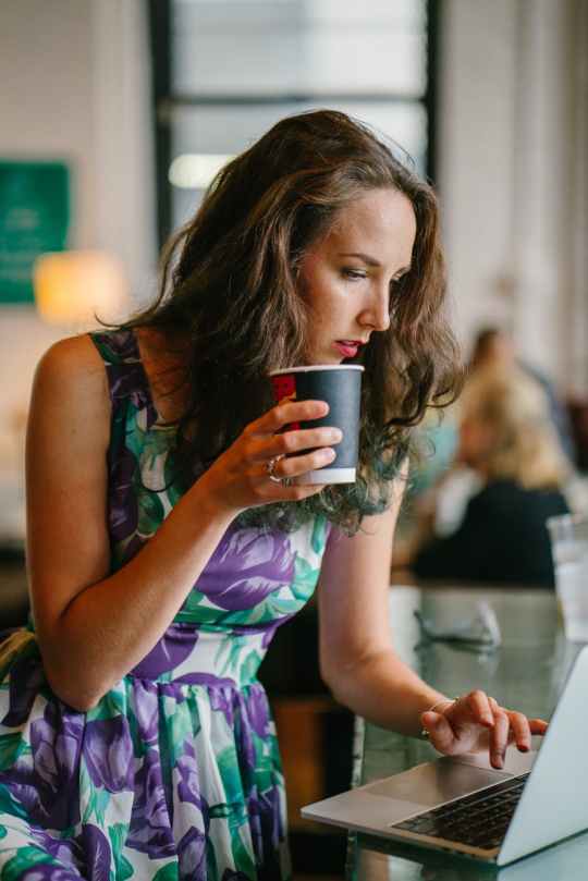 selective focus photography of woman holding disposable cup using gray laptop on table